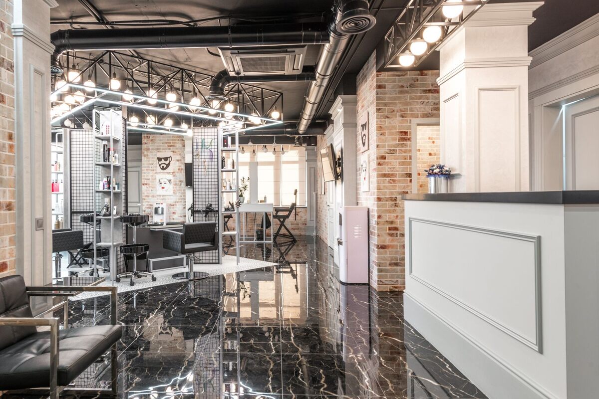 Illustration: the empty reception counter of a small salon, with styling chairs, mirrors and a product shelf behind it and nobody in the room.