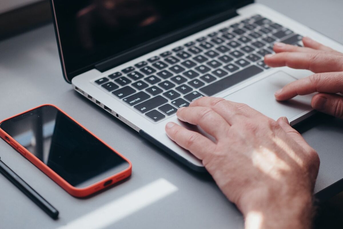 Illustration: a tidy desk with an open laptop, a smartphone and a pen beside it; only the owner's hands are visible, typing on the keyboard.