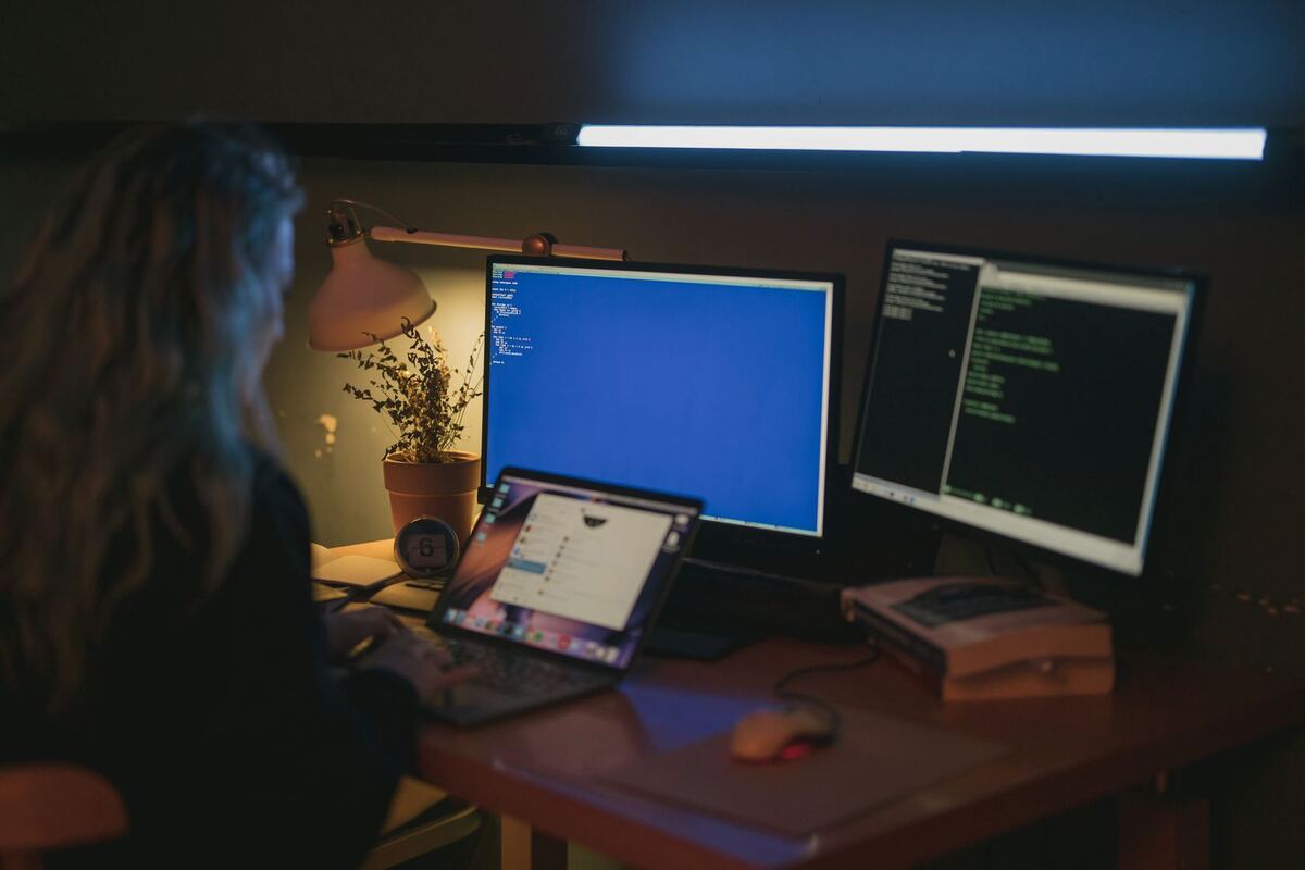 A person working at a desk with two monitors in a dim room