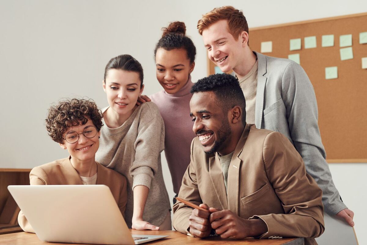 Five colleagues gathered around one laptop, smiling